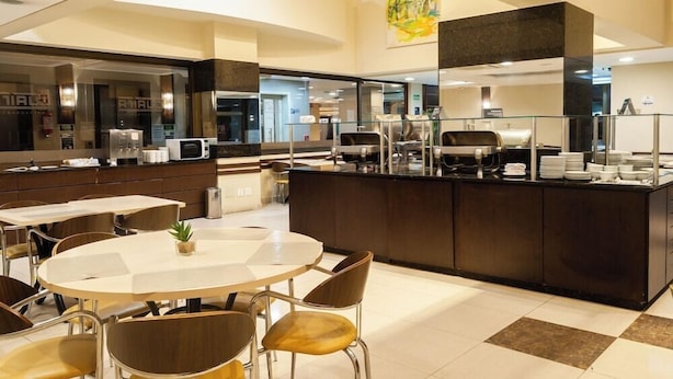 A modern hotel lobby with a central island counter, seating area, and a large abstract painting on the wall. - Master Express Curitiba (Curitiba)