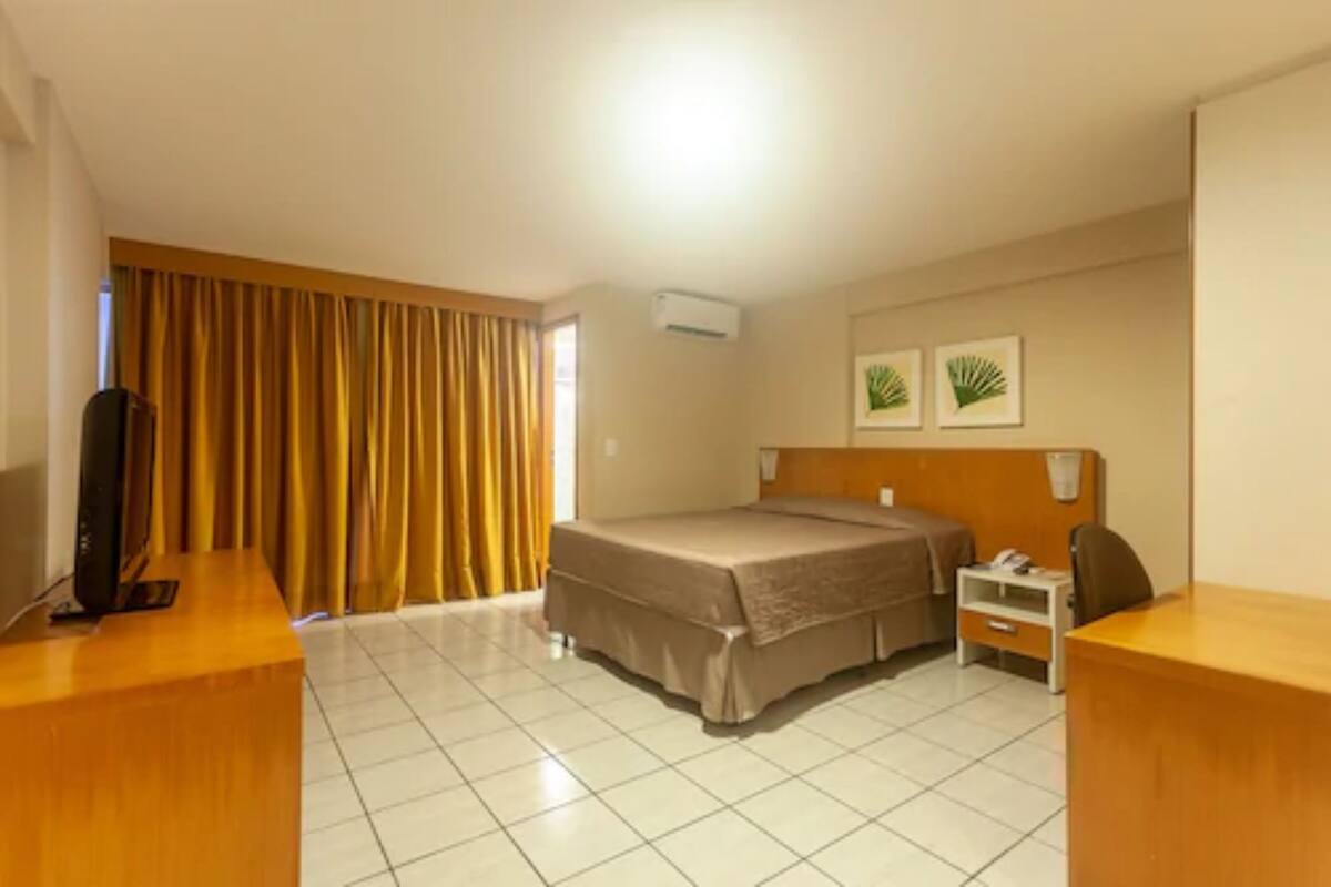 Ein Hotelzimmer mit Bett, Schreibtisch, Stuhl, Fernseher, Nachttisch und Vorhängen.
