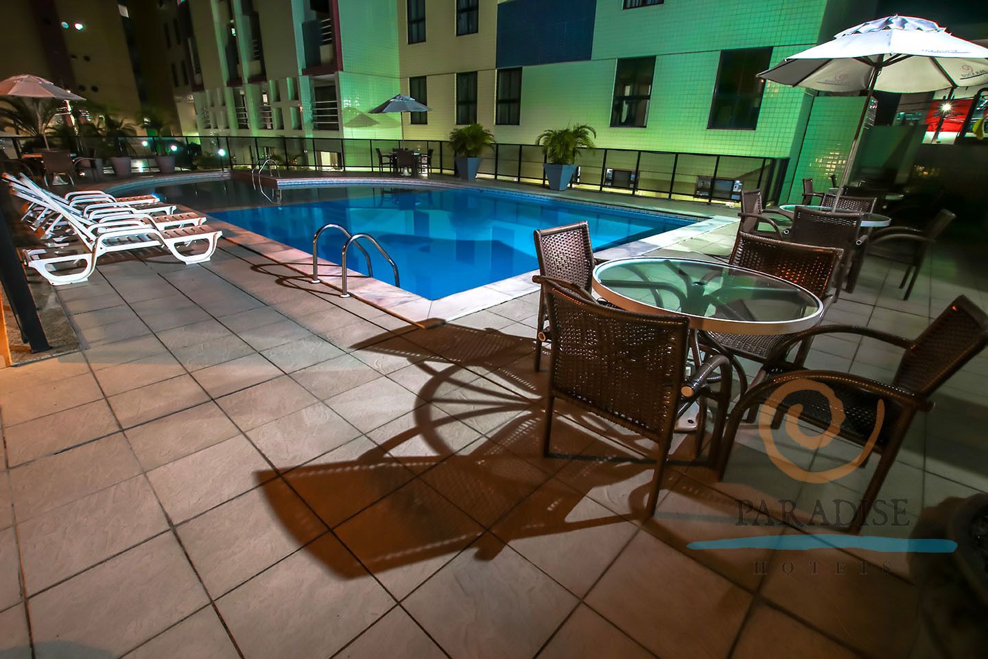 A swimming pool area with lounge chairs and a table, surrounded by a tiled deck.