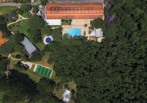 An aerial view of a property with a swimming pool, tennis court, and a large building with a red roof.