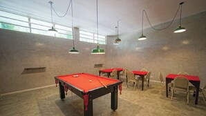 A room with a pool table, chairs, and tables with red tops.
