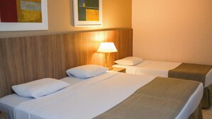 A hotel room with two single beds, a nightstand with a lamp, and a wooden headboard.
