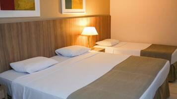 Quarto de hotel com duas camas de solteiro, uma mesa de cabeceira com abajur e cabeceira de madeira.