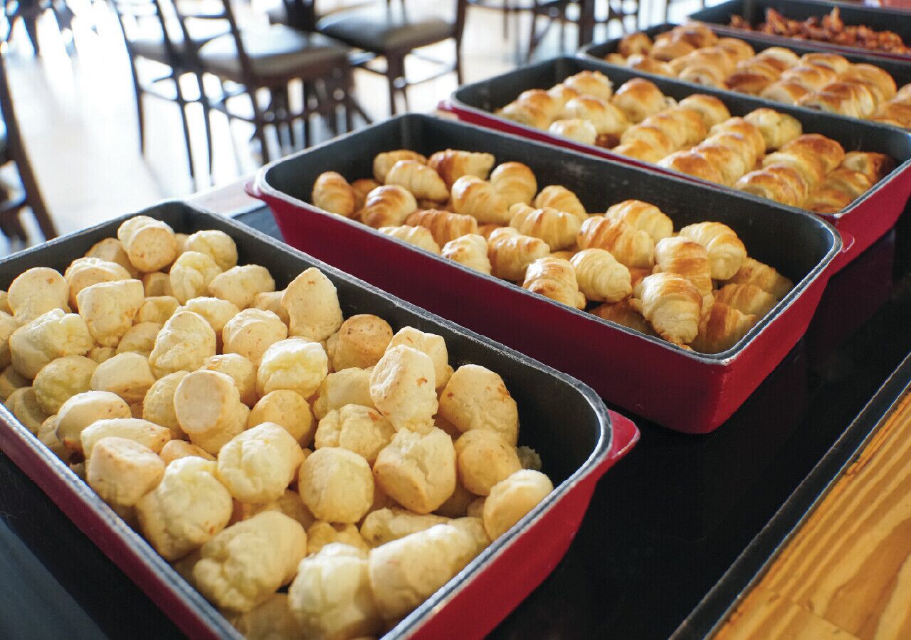 Buffet com bandejas de comida, incluindo pães e doces.