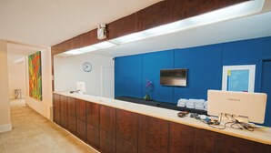 A reception area with a wooden counter, a clock, a Samsung monitor, and a blue wall.