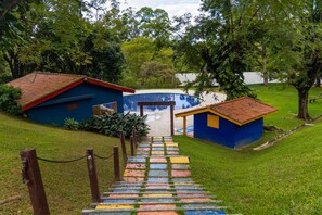 Un sendero que conduce a un edificio de fachada azul y tejado rojo, rodeado de abundante vegetación.