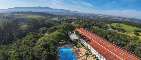 A hotel with a swimming pool, surrounded by lush greenery and a red-roofed building.