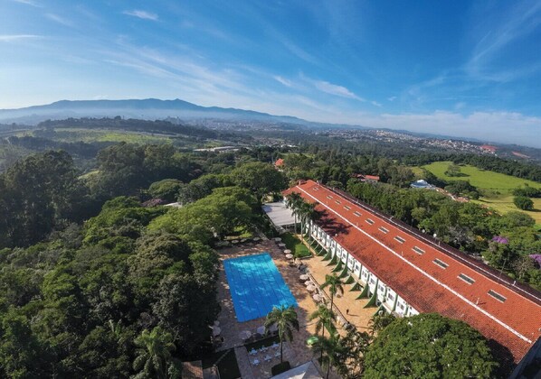 A hotel with a swimming pool, surrounded by lush greenery and a red-roofed building.