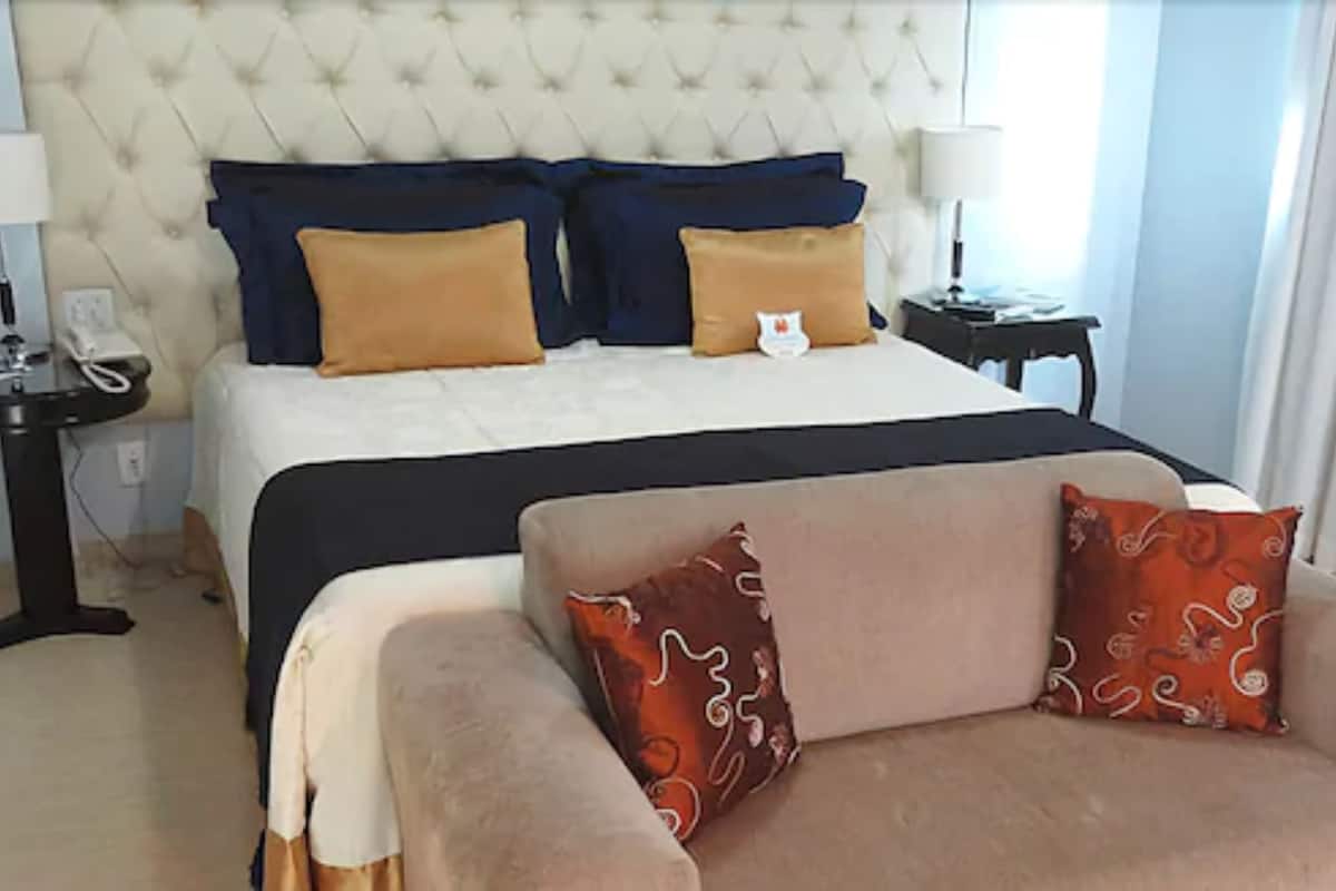 Ein Hotelzimmer mit einem großen Bett, zwei Nachttischen, einer Lampe und einem Sofa mit gemusterten Kissen.