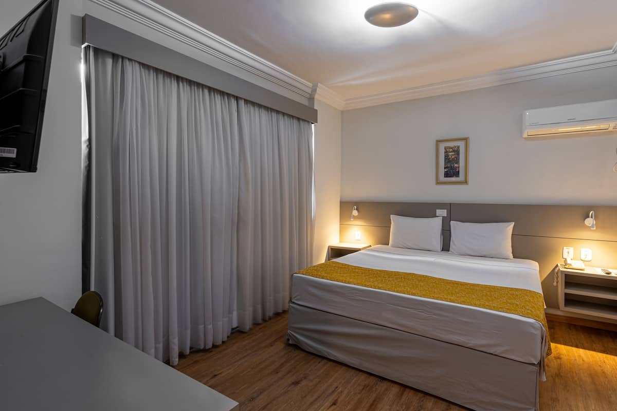 Ein Hotelzimmer mit Bett, Vorhängen, Nachttisch, Lampe und Klimaanlage.