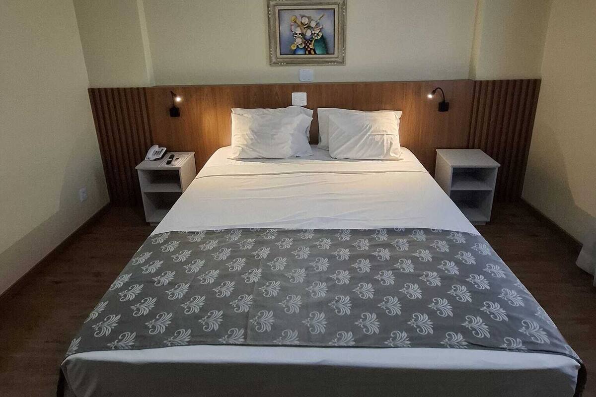 Ein Hotelzimmer mit einem großen Bett, zwei Nachttischen, einem Telefon und einem gerahmten Bild an der Wand.
