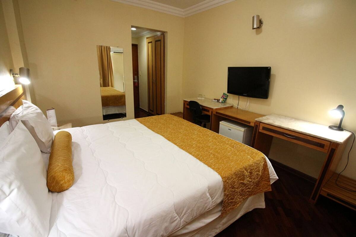 Ein Hotelzimmer mit einem Bett, einem Schreibtisch, einem Sessel, einem Fernseher und einem Spiegel.