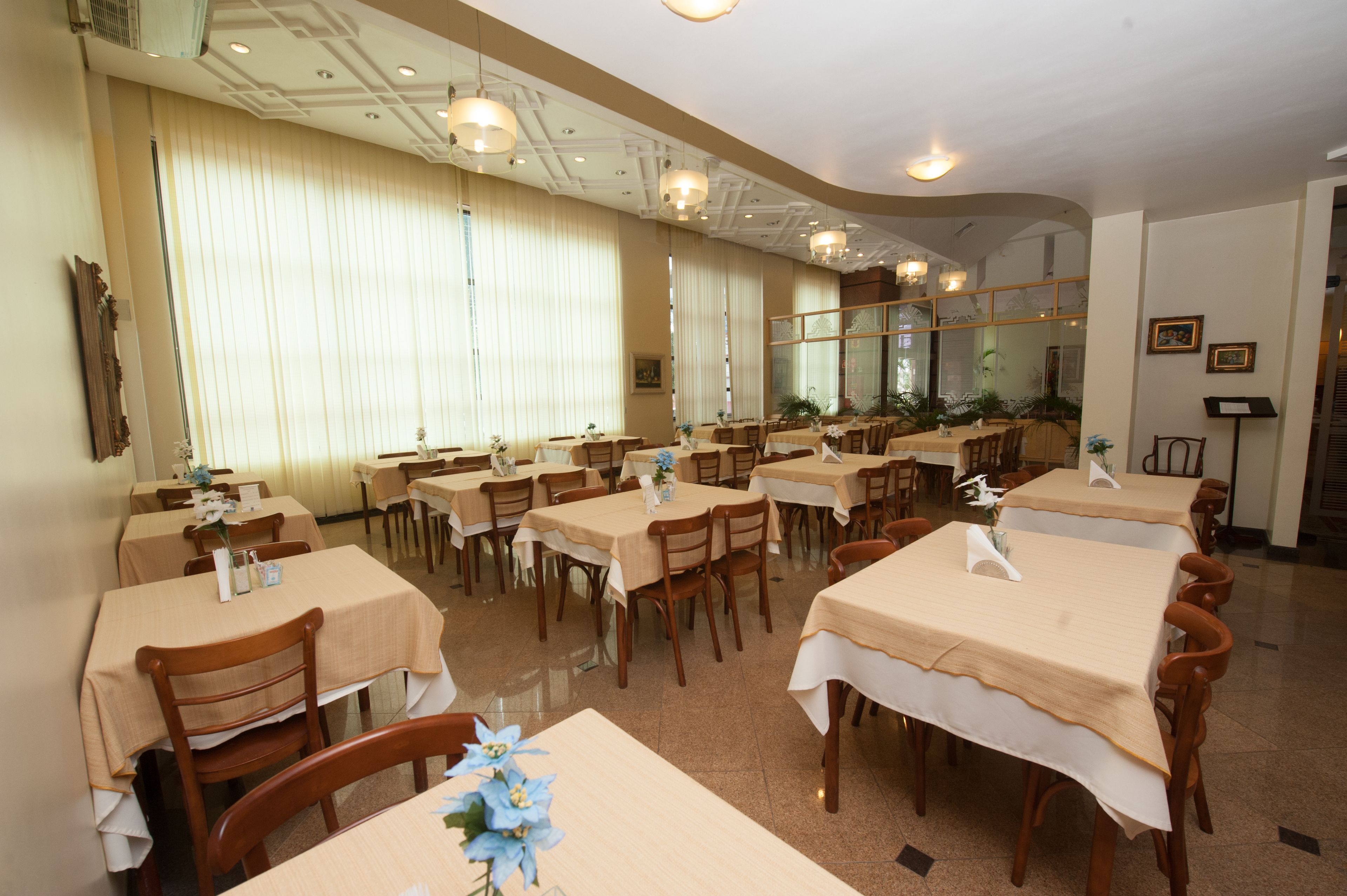 A restaurant with multiple tables and chairs, arranged in a spacious dining area with large windows and ceiling lights.