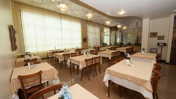 A restaurant with multiple tables and chairs, arranged in a spacious dining area with large windows and ceiling lights.