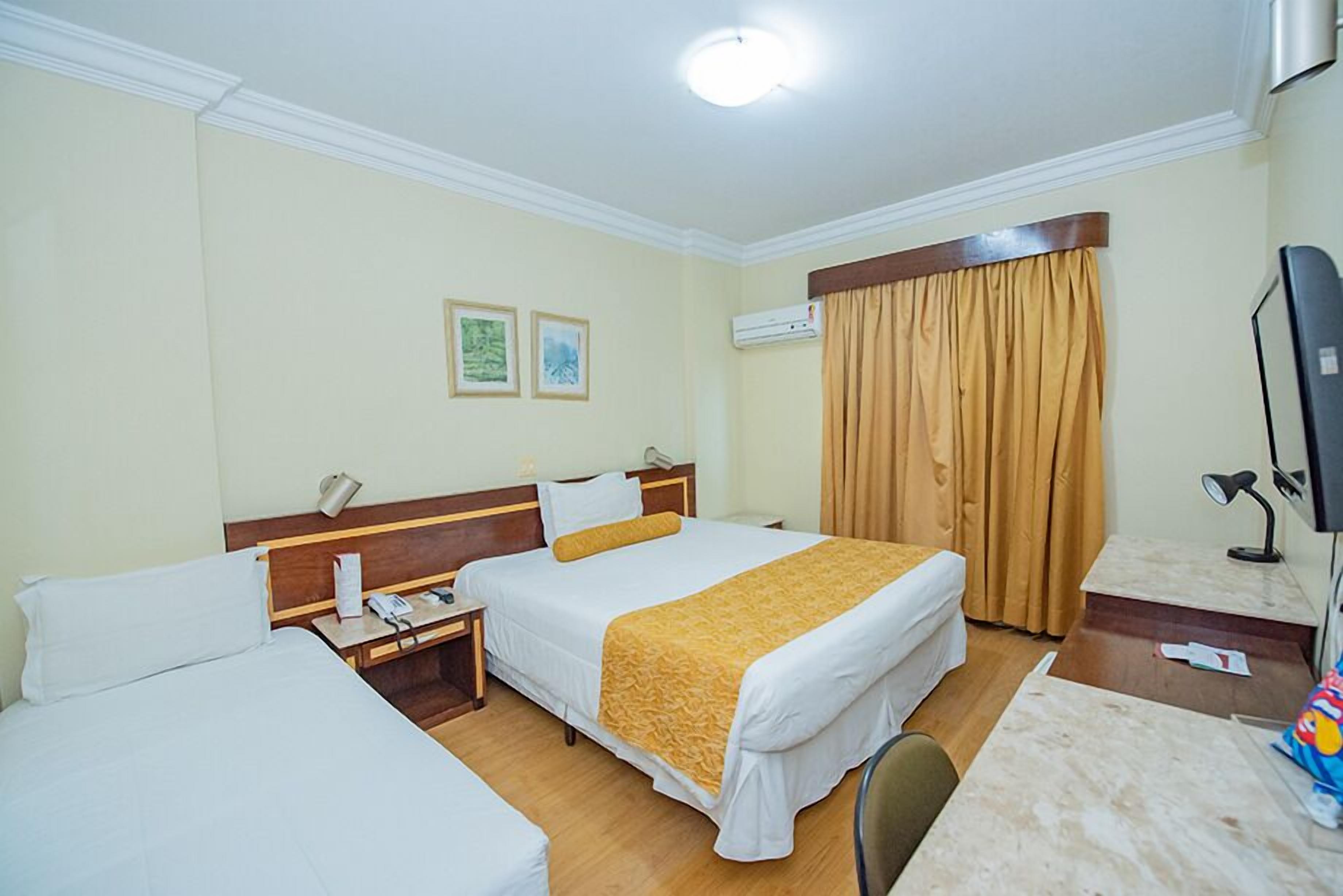 A hotel room with two beds, a desk, a chair, an air conditioning unit, and a television.