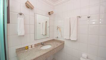 A bathroom with a sink, mirror, towel rings, and a toilet.