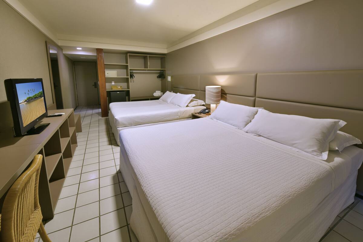 Habitación de hotel con dos camas, un escritorio con televisor y un baño visible a través de una puerta abierta.