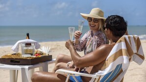 Una pareja sentada en sillas de playa, con una bandeja de comida y bebidas, mirando al océano.