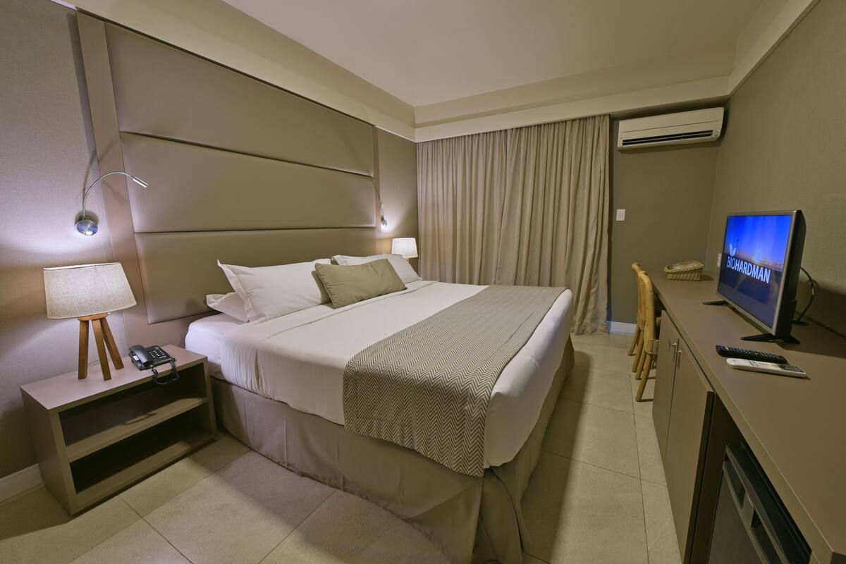 Habitación de hotel con una cama grande, lámparas de noche, un televisor, un escritorio con lámpara y una silla.