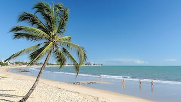 Na praia, areia branca, espreguiçadeiras, guarda-sóis