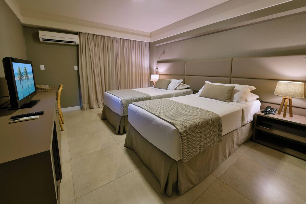 Habitación de hotel con dos camas, televisor, escritorio con computadora y aire acondicionado.