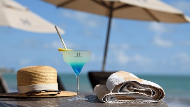 Un vaso de martini con una pajita sobre una mesa, un sombrero de paja y una toalla doblada.