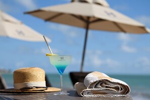 Un vaso de martini con una pajita sobre una mesa, un sombrero de paja y una toalla doblada.