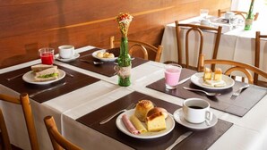 A dining area with tables set for breakfast, including sandwiches, pastries, and beverages.
