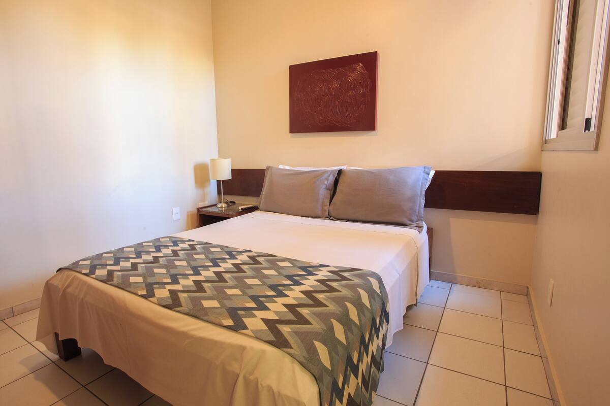 Una camera d'albergo con un letto, un comodino, una lampada e un quadro appeso al muro.