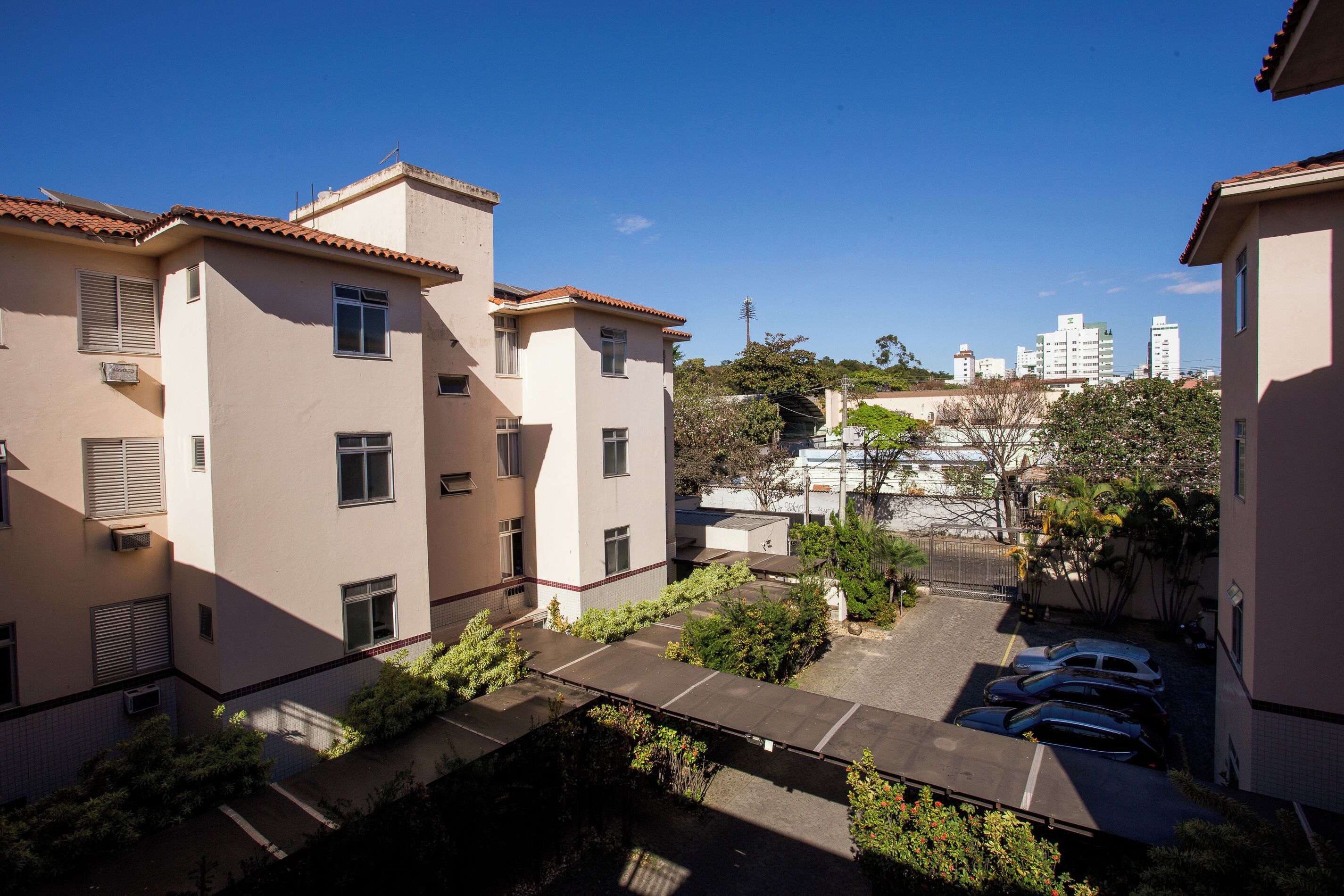 A residential building with multiple floors, a parking area, and a view of taller buildings in the background.