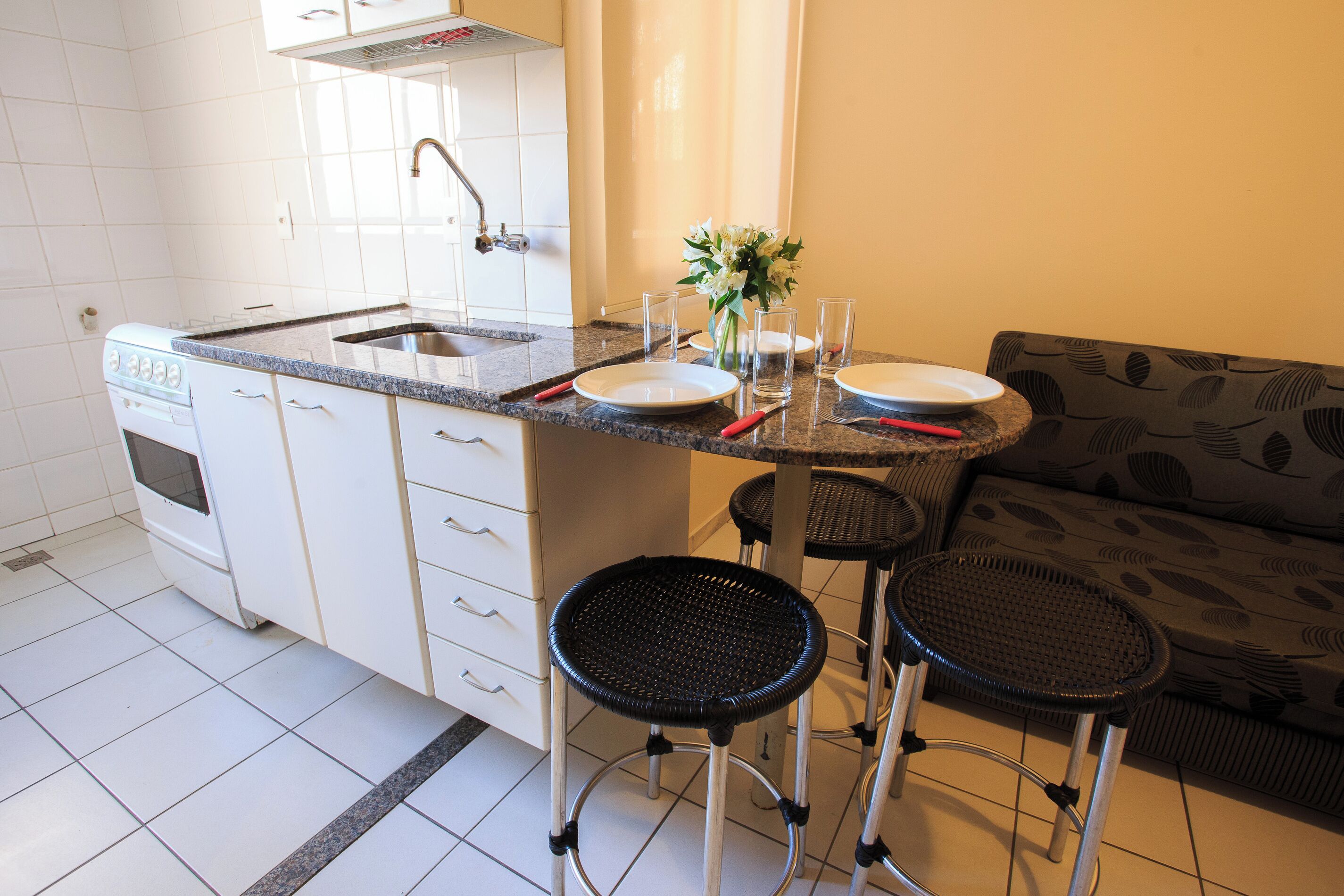 A compact kitchen with a sink, stove, and a dining area with stools and a table set for two.