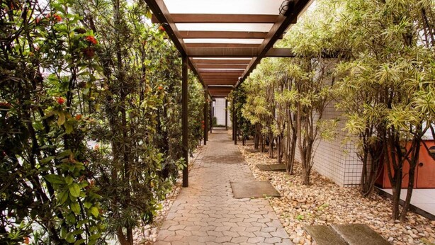 A covered pathway flanked by lush greenery and a tiled wall.