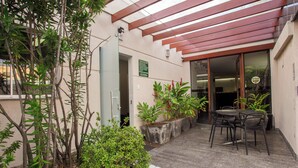 A covered outdoor seating area with a table and chairs, surrounded by potted plants and a pergola.