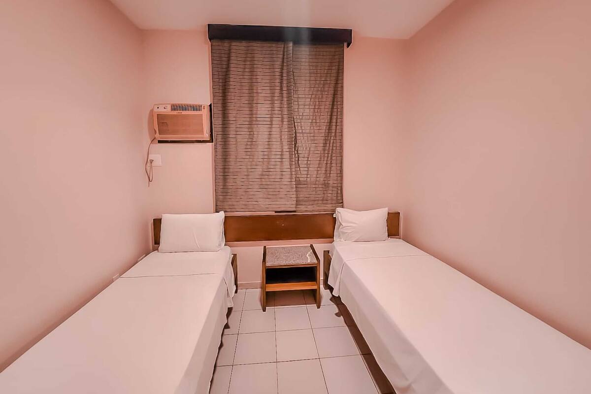 Una camera piccola e pulita con due letti singoli, un comodino in legno, un tavolino e una radio fissata al muro.