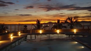 Un área de piscina con vista al atardecer, rodeada por una barandilla y plantas en macetas.