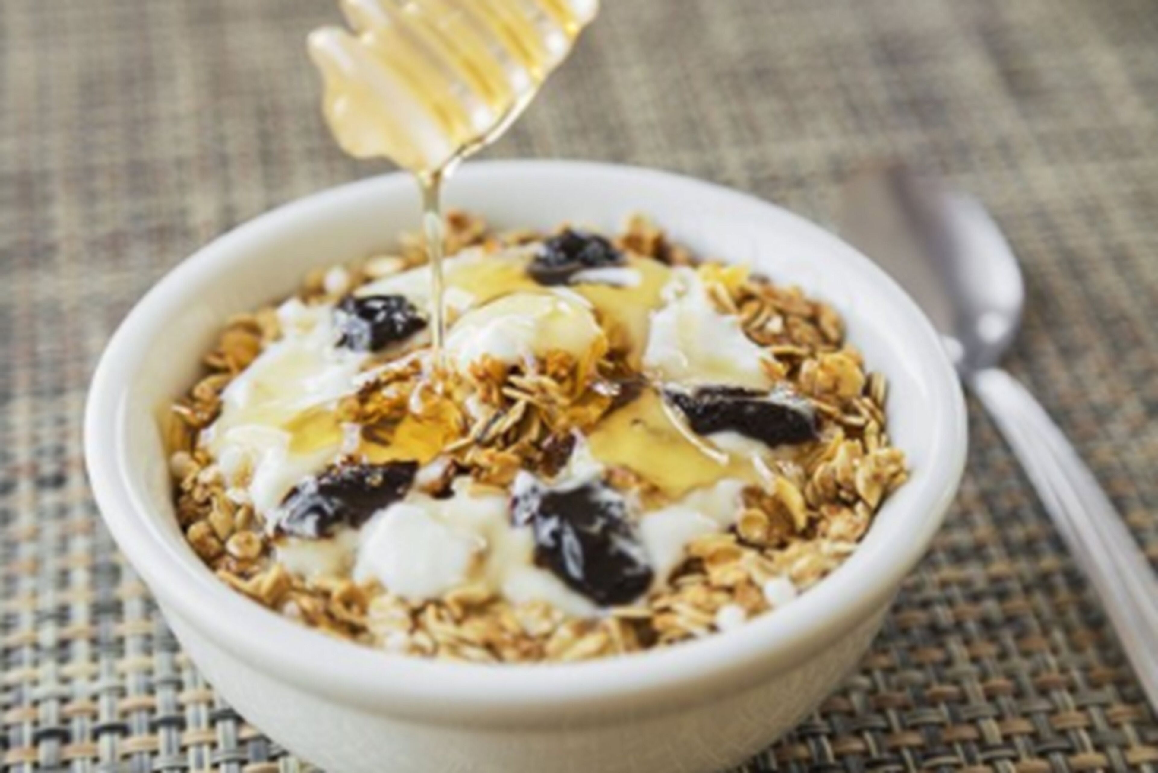 Un bol de granola amb iogurt i mel, amb la mel abocant-se a sobre.