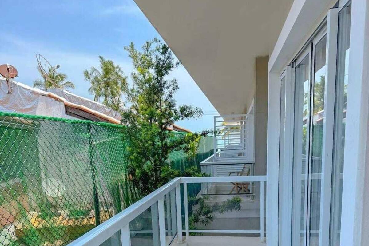A balcony with a glass railing, a tiled floor, and a view of a green fence and trees.