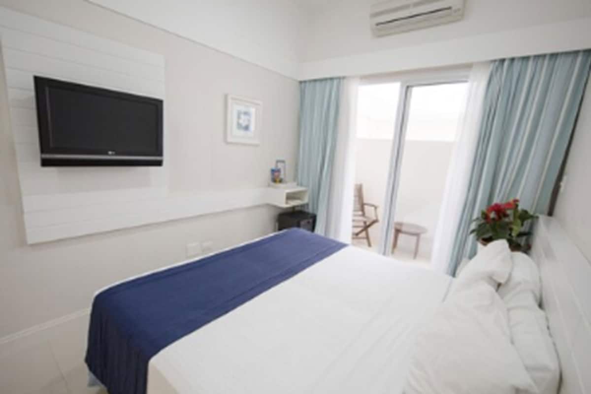 A hotel room with a bed, a TV mounted on the wall, a small table, and a chair.