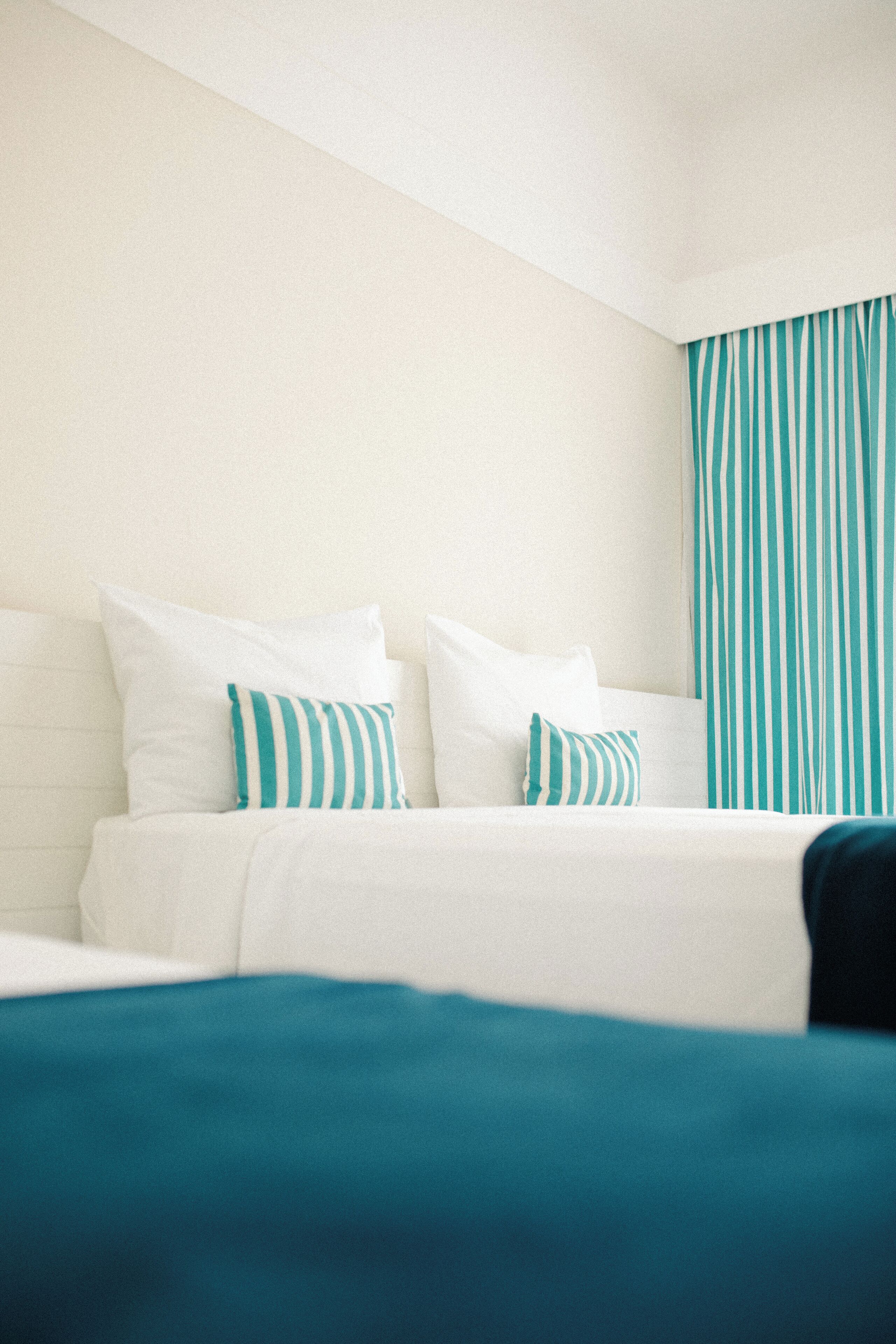 Una habitación de hotel con una cama, ropa de cama blanca y cortinas a rayas.