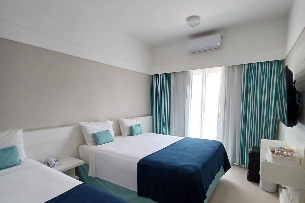 A hotel room with two beds, a desk, a chair, a TV, and a window with curtains.