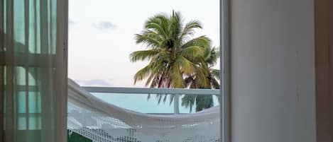 Vista desde una habitación con cortina blanca, pared de azulejos verdes y una palmera afuera.
