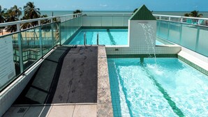 A rooftop pool with clear blue water, a tiled deck, and a view of the ocean. - Rede Andrade Solmar (João Pessoa)