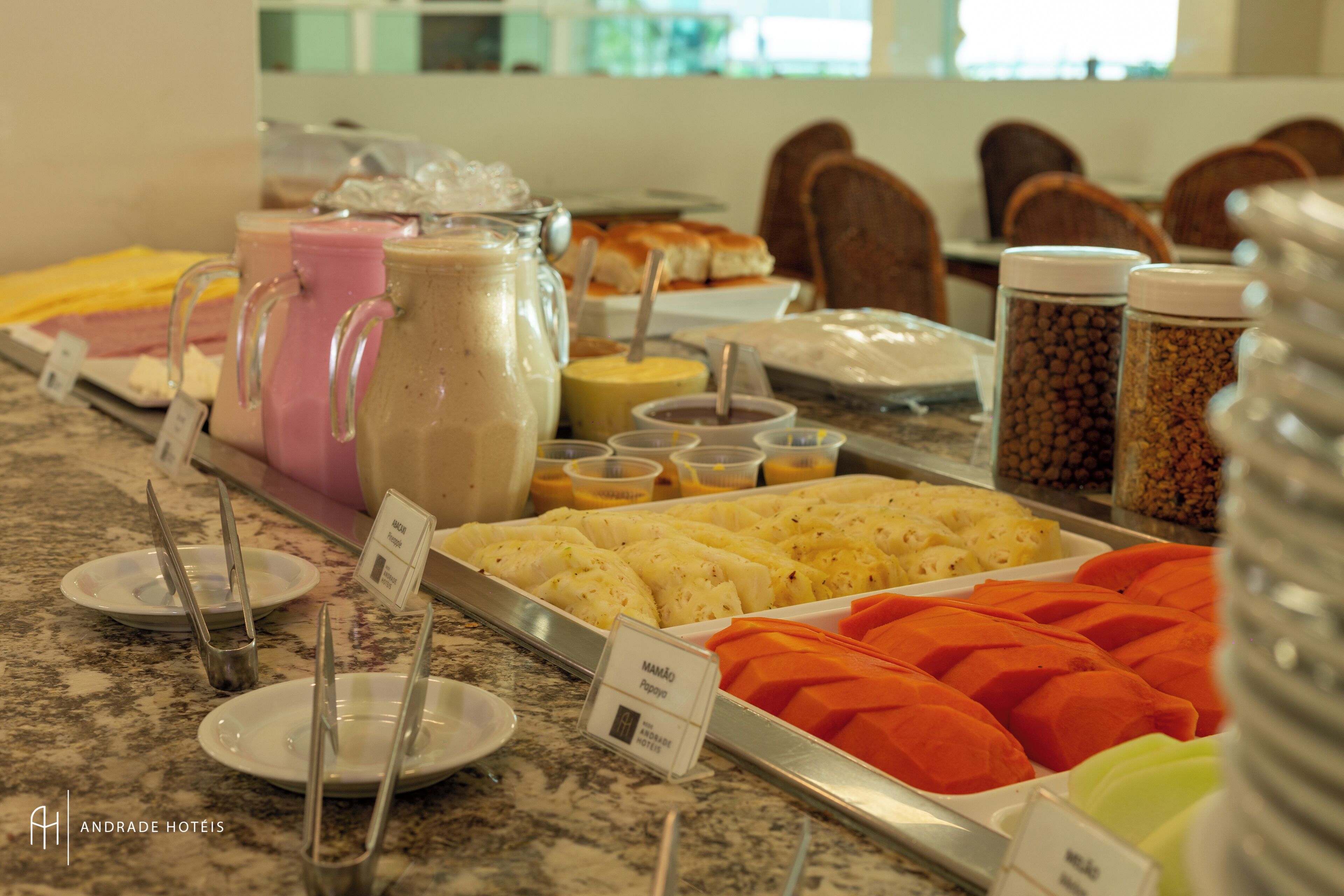A buffet with various food items and beverages, including a large pitcher of a pink beverage, a container of orange fruit, and several small bowls with different toppings.