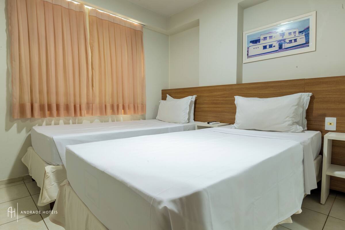 A hotel room with two single beds, a wooden headboard, a nightstand, and a framed picture on the wall.