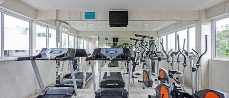 Uma academia com esteiras, elípticos e bicicletas ergométricas.