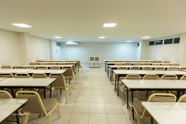 A conference room with rows of tables and chairs, a podium, and a whiteboard.