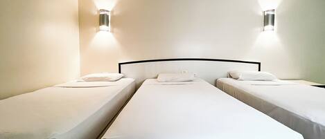 A hotel room with three single beds aligned in a row, each with a white mattress and pillow.