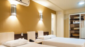 Habitación de hotel con dos camas, una mesita de noche con teléfono y un armario con ropa colgada.