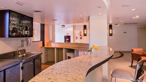 Un moderno hall de hotel con barra curva, zona de estar y cocina a la vista.