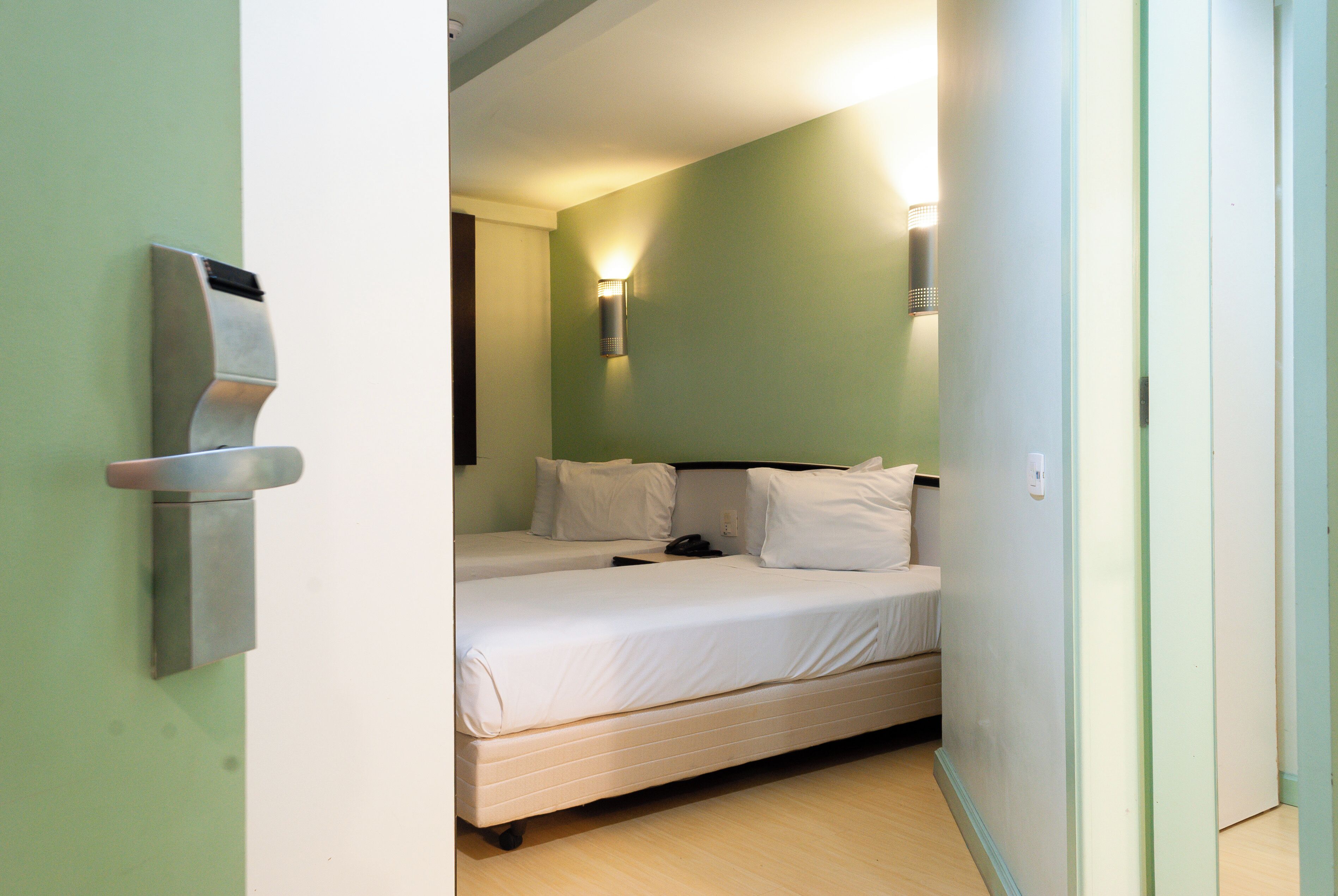 A hotel room with a bed, a wall-mounted light, and a door.